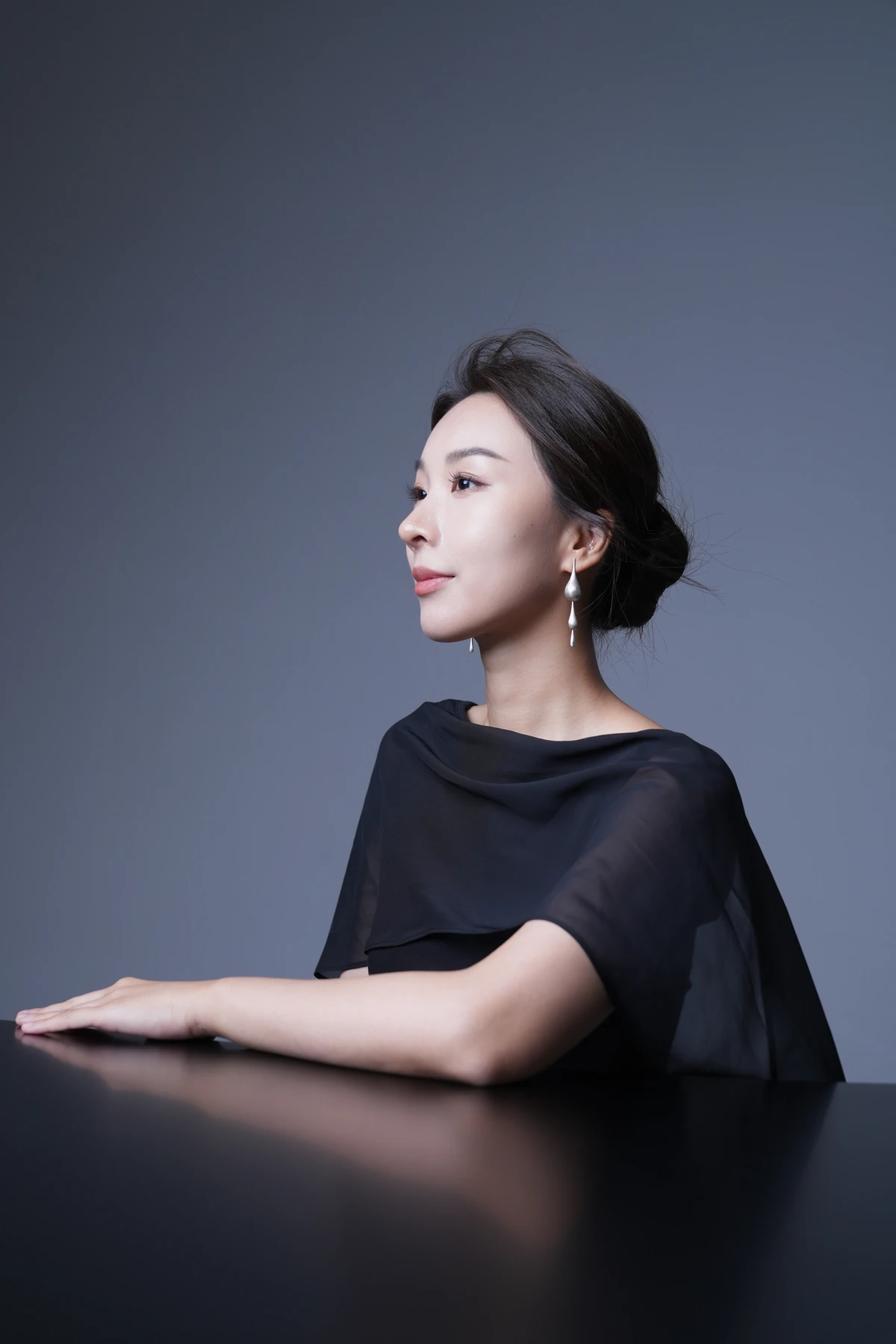 Ningjialu (Lulu) Liu wearing black, with one arm resting on a piano against a gray background.