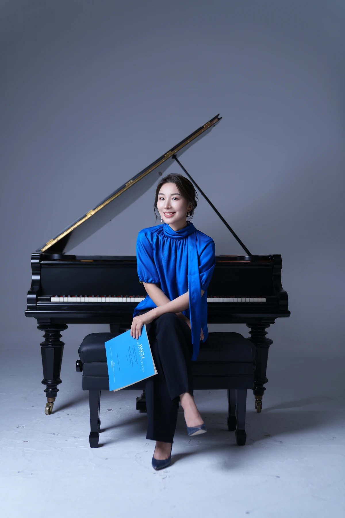 Ningjialu (Lulu) Liu in a blue blouse, seated in front of a grand piano and holding a score.